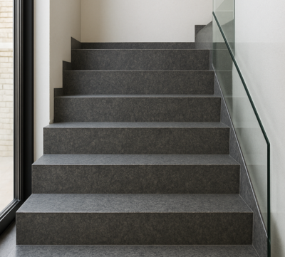 Escalera de piedra gris con barandilla de cristal, iluminada con luz natural.